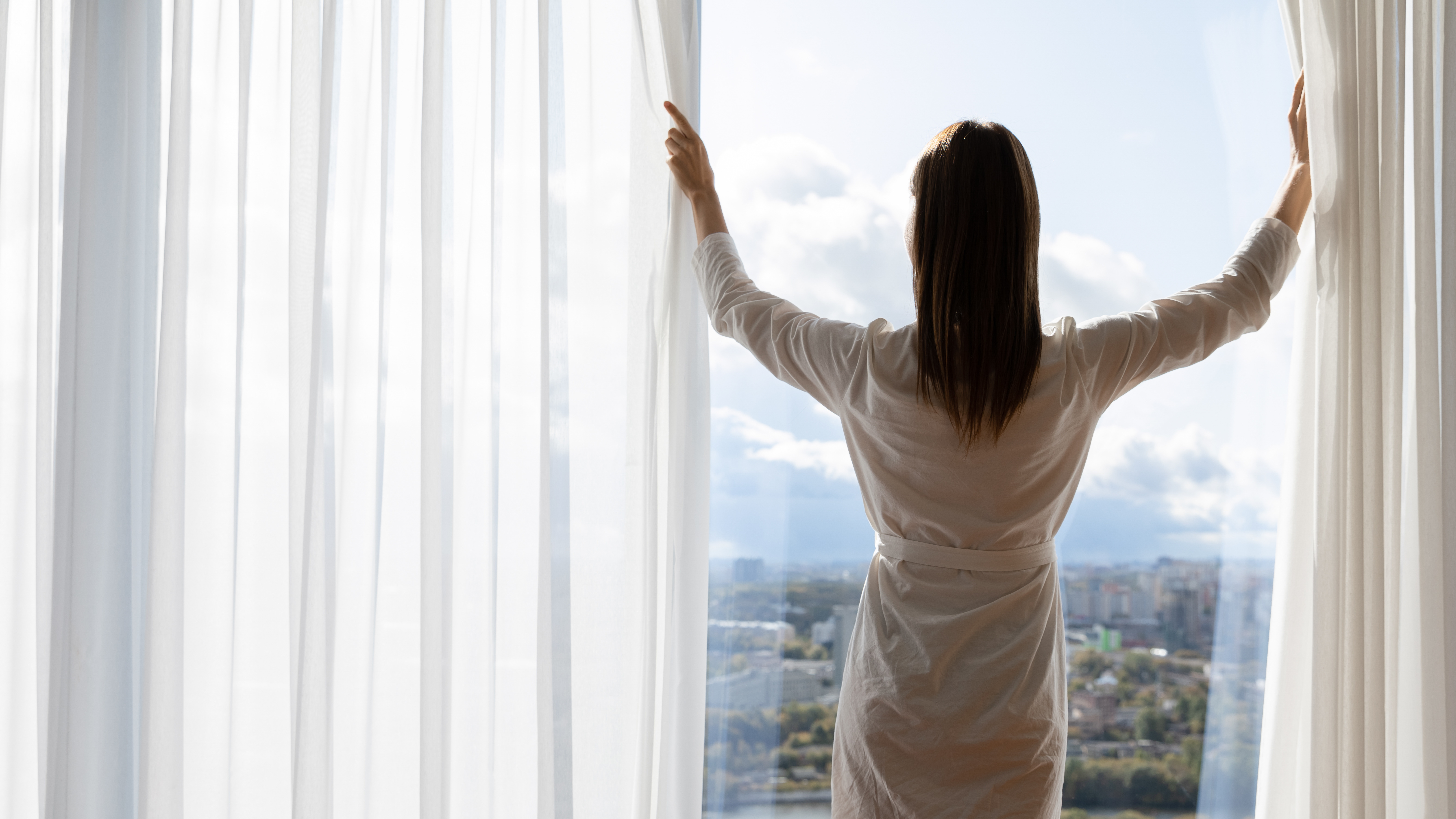 Rich young woman wear gown open curtains stand at window